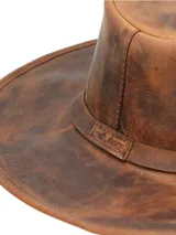 Sombrero de cuero marrón con efecto envejecido, ala ancha y copa con pliegue central. Presenta dos orificios de ventilación a cada lado de la copa y una banda de cuero simple alrededor de la base.