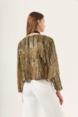 Saco corto dorado con flecos, bordado con lentejuelas y detalles en canutillo, con escote en V y mangas largas.