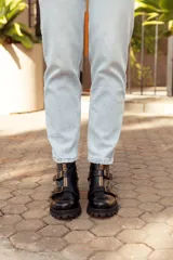 Botas de cuero negras con suela track, cierre frontal dorado y dos hebillas decorativas en el empeine.