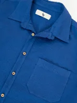Camisa azul de manga corta confeccionada en algodón ligero con textura waffle. Presenta corte cuadrado, bolsillo en el pecho y botones de coco grabados con el logo de Polonio.