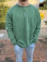 Buzo verde con cuello redondo y logo pequeño bordado en el pecho.