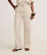 Pantalón largo de cintura alta color beige, confeccionado en tejido viscolino, con trabillas en la cintura, cinturón de cuerda para lazo, cierre tradicional y pliegues.