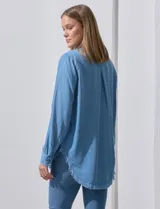 Camisa de jean celeste con flecos en el ruedo, de mangas largas y corte recto.