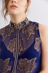 Camisa larga sin mangas confeccionada en viscosa azul con estampado de flores doradas y cuello mao. Presenta bordados en cuello y cartera frontal, y cierre frontal con cremallera.