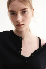 Saco corto negro de punto fino suave con cuello redondo, mangas cortas y botonadura frontal. Tiene ribete festoneado en tapeta, mangas y bajo.