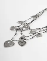 Collar de múltiples hebras negras con dijes colgantes de metal plateado en forma de corazón, algunos lisos, otros con textura o incrustaciones de piedras negras y transparentes.