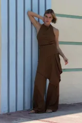 Pantalón marrón de tiro medio con cintura elástica y pierna ancha. Presenta una superposición tipo pareo ajustable con lazadas.