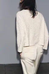 Chaqueta color crema de tejido de punto con lentejuelas, cuello barco, manga larga y cierre frontal con botones.