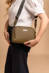 Bandolera pequeña de textura símil cuero color caramelo/marrón, con dos compartimentos principales con cierre. Correa ancha ajustable de tela negra con inscripción en relieve.