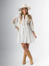 Vestido corto blanco de algodón italiano con bordado azul, mangas tres cuartos y botones frontales.