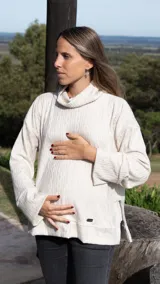 Sweater tejido color crema con cuello alto y mangas largas. Tiene corte oversize y aberturas laterales con cierres invisibles verticales para amamantar.