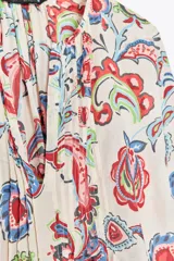 Camisa de algodón color crudo con estampado de cachemir en tonos rojo, azul y verde. Tiene cuello redondo, escote en pico, manga tres cuartos acampanada y bajo asimétrico redondeado.