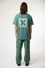 Remera de manga corta color gris oscuro, con cuello redondo y un pequeño parche cuadrado con una 'X' estampada en el pecho izquierdo.