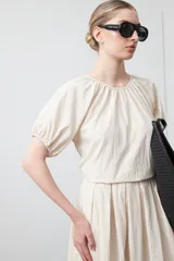 Top negro de manga corta con escote redondo y frunces en la costura de la sisa, creando un efecto de manga abullonada. El tejido parece ligero y con textura.