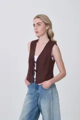 Chaleco sin mangas color marrón oscuro, de corte ajustado al cuerpo, con escote en V y cierre frontal mediante lazos anudados con detalles de cuentas oscuras.