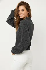 Sweater de tejido de punto grueso color blanco roto, con cuello redondo y mangas largas abullonadas. El calce es holgado y corto (cropped).