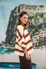 Remera de algodón y poliéster a rayas horizontales rojas y azul marino sobre fondo crudo. Tiene cuello tipo polo con botones, mangas amplias y corte oversized.