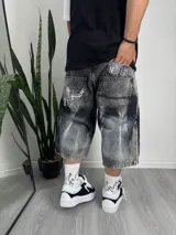 Bermuda de jean gris con efecto lavado, corte ancho, largo a la rodilla y bolsillos traseros con logo de New Era y esqueleto estampado.