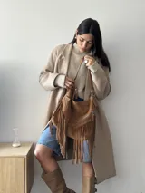 Bolso tipo hobo color tostado, hecho de cuero con flecos largos en el frente y dos bolsillos con cierre. Tiene una manija regulable con hebillas metálicas.