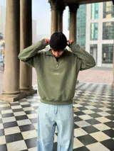 Buzo verde militar de felpa con frisa gruesa, corte boxy, medio cierre con cremallera y estampado minimalista con la frase "The Wise Club Exclusive Members".