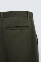 Pantalón verde oscuro de corte amplio confeccionado en tejido de lyocell. Presenta pliegues frontales, bolsillos laterales y traseros de ojal. Cierre frontal con cremallera y botón.