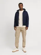 Campera híbrida Jack & Jones color azul marino, ligera y resistente al agua, con capucha, mangas largas con puños elásticos, cierre con cremallera y bolsillos frontales con cierre. Relleno de fibra sintética tipo plumón.