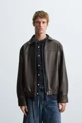 Cazadora bomber de efecto piel color marrón oscuro, con cuello solapa, cierre frontal de cremallera, bolsillos de vivo en cadera y bajo elástico.