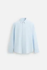 Camisa celeste de algodón con textura jacquard, corte relaxed fit, cuello solapa, manga larga con puños abotonados y cierre frontal con botones.