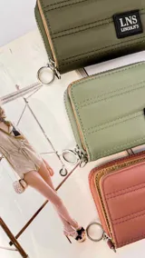 Billetera corta con cierre alrededor y tapa, confeccionada en tela capitoneada. Incluye varias reparticiones con tarjeteros y bolsillos internos, y una correa de mano desmontable. Disponible en negro, rojo y dorado.