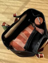 Bolso negro tipo tote de neopreno con bolsillo interno de red, sobre haciendo juego y gancho para sujetarlo.