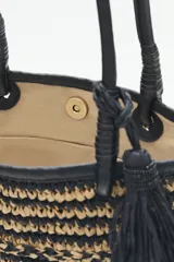 Bolso tote tejido en raffia color negro y beige, con vivos y correas en cuero sintético negro. Tiene cierre interno con snap metálico y forro de algodón.