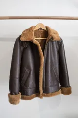 Campera gamulán marrón con cuello, puños y ruedo de piel sintética. Cierre frontal con cremallera y bolsillos laterales.