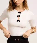Blusa blanca de mangas cortas, confeccionada en Rib, con cuello redondo y lazos de terciopelo negros uniendo la abertura en la parte de abajo.