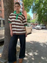 Remera oversize a rayas horizontales marrones y blancas, con cuello polo y mangas cortas con ribete verde.