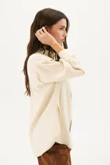 Camisa beige de corte recto, con cuello clásico, cierre frontal con botones, bolsillo en el pecho y mangas largas con puños abotonados.
