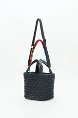 Cartera tote azul de nylon matelassé con diseño de corazones. Tiene manijas cortas y dos correas desmontables, una de cuero sintético y otra de tela trenzada multicolor. Cuenta con cierre superior y dos bolsillos internos.