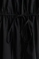 Blusa sin mangas color negro en tejido liviano de algodón con escote en V y costuras fruncidas en los hombros. Frente abierto con tres tiras finas, dos con efecto fruncido.