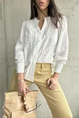 Camisa blanca de manga larga con detalles de broderie y calados en el frente y las mangas. Tiene cuello mao y cierre frontal con botones. Los puños son elásticos.