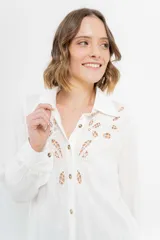 Camisa blanca de voile con bordados calados en el frente, cuello camisero, mangas largas con puños abotonados y cierre frontal con botones. 