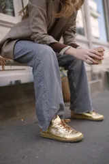 Championes deportivos de cuero y gamuza color dorado metalizado y marrón. Suela de caucho color crema con línea roja. Cordones color crema.