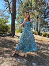 Vestido largo de seda con estampado floral en tonos celeste, verde y azul. Tiene escote en V y mangas cortas.