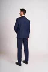 Traje de vestir azul marino, compuesto por saco de dos botones con solapa de muesca, dos bolsillos laterales con solapa y un bolsillo de ojal en el pecho, y pantalón de vestir con corte recto. Incluye camisa blanca, corbata celeste y pañuelo de bolsillo blanco con borde celeste.