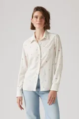 Camisa de lino color blanco hueso con estampado floral en tonos marrones. Tiene cuello clásico, cierre frontal con botones y mangas largas con puños abotonados.