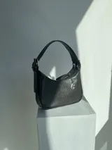 Cartera negra de cuero sintético con textura croco, para usar al hombro. Tiene hebillas metálicas para regular el largo de la correa, cierre YKK, dije metálico con el logo de la marca y forro interior.