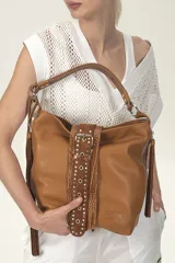 Cartera tipo hobo de cuero color tostado con detalles de cuero croco al tono, flecos laterales y tira de gamuza con tachas metálicas en el frente. Tiene doble asa, cierre metálico y correa larga regulable y desmontable.