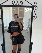 Minifalda negra de jean con tablas, abertura lateral y cinturón con hebilla metálica.