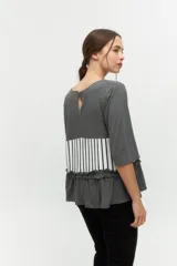 Remera gris con mangas 3/4, corte recto y detalle de volados en el ruedo. Presenta una franja horizontal con estampado de rayas verticales blancas y negras.