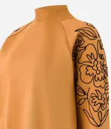 Sweater color ocre con cuello alto y mangas largas con sisas raglán. El sweater tiene bordados de flores en los laterales de las mangas.
