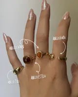 Set de cuatro anillos dorados con diferentes diseños: uno con piedra marrón cuadrada, otro con piedra naranja redonda, uno liso con forma de esfera y uno liso con forma de cilindro.