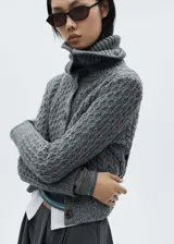 Cárdigan gris de tejido de punto grueso con diseño trenzado, cuello camisero, cierre frontal con botones y terminaciones acanaladas.